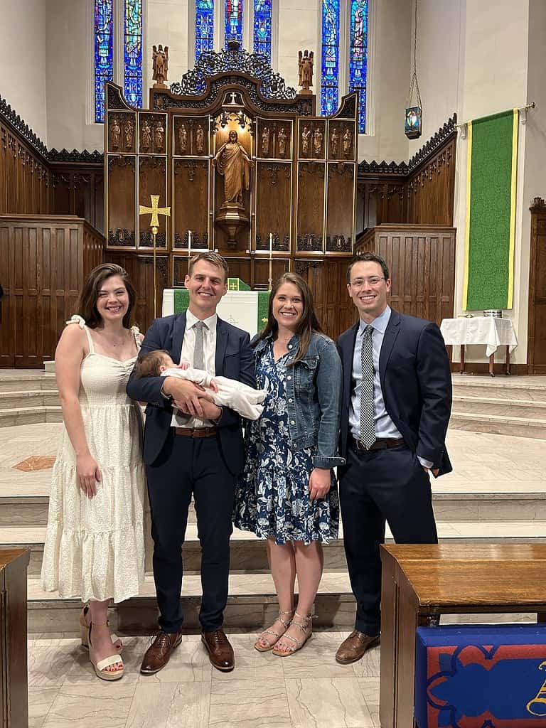This is a group photo taken at Mason's son's baptism inside First Lutheran Church. It includes, from left to right, Mason's wife, Mason holding his son, and Allison and Adam Guthmiller, his son's godparents.